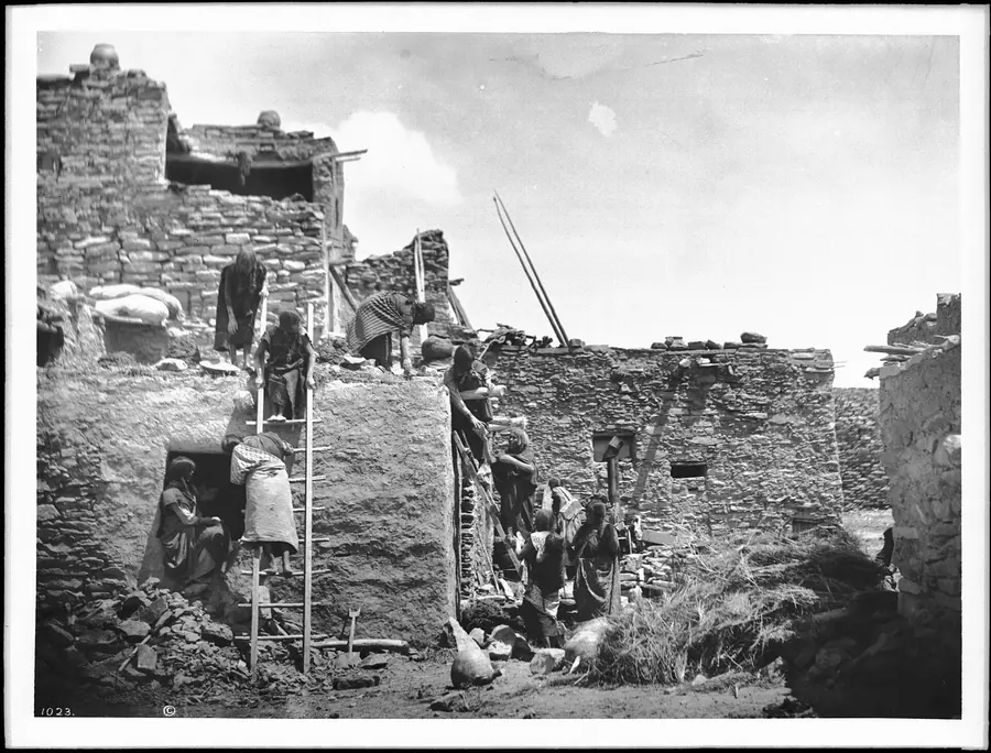 Photograph of women laying stone and mud courses on a pueblo wall.