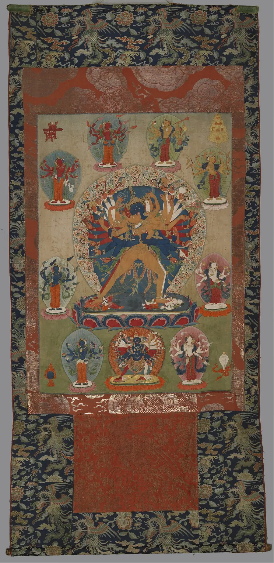 Tibetan thangka with a many-armed blue central deity surrounded by ranked figures.