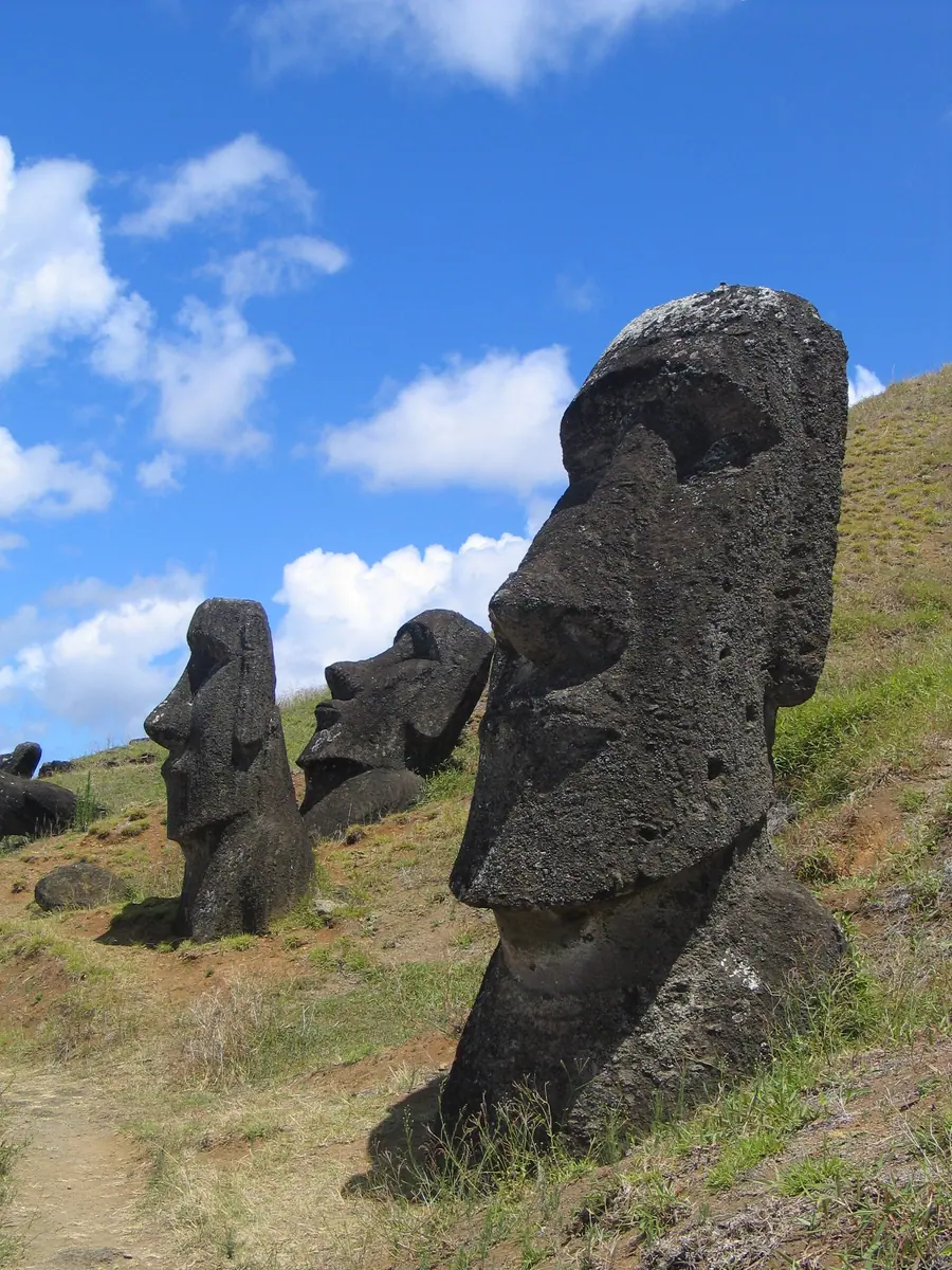 Row of massive carved stone heads half-buried on a grassy slope.