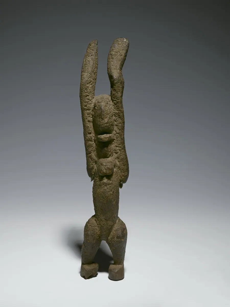 Elongated dark wooden figure with both arms raised vertically.