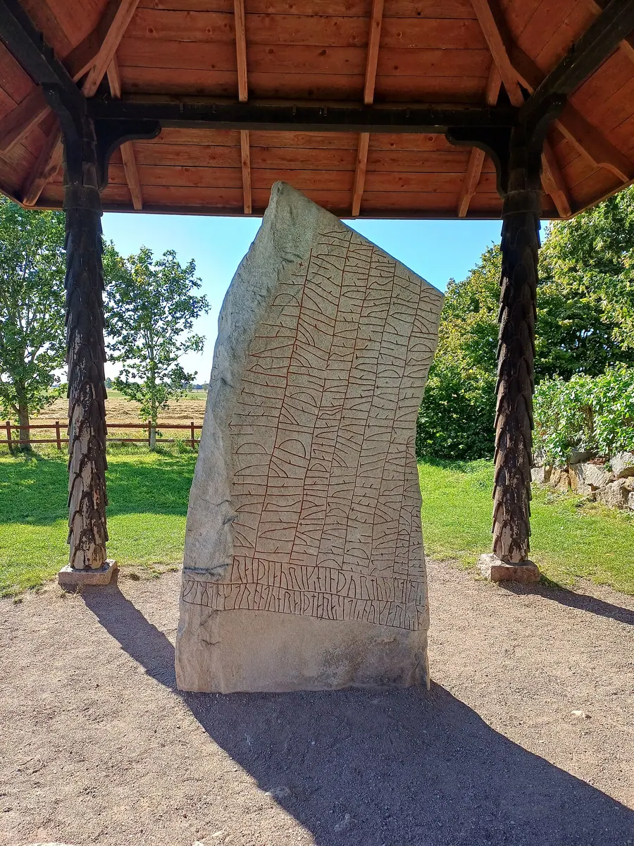 Tall granite runestone densely covered in runic inscription on every face.