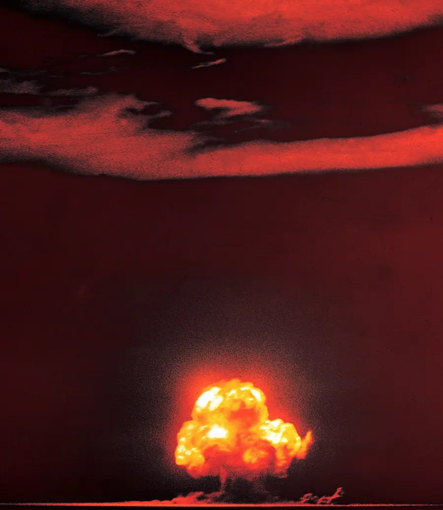 Colour photograph of an early nuclear fireball rising over desert.